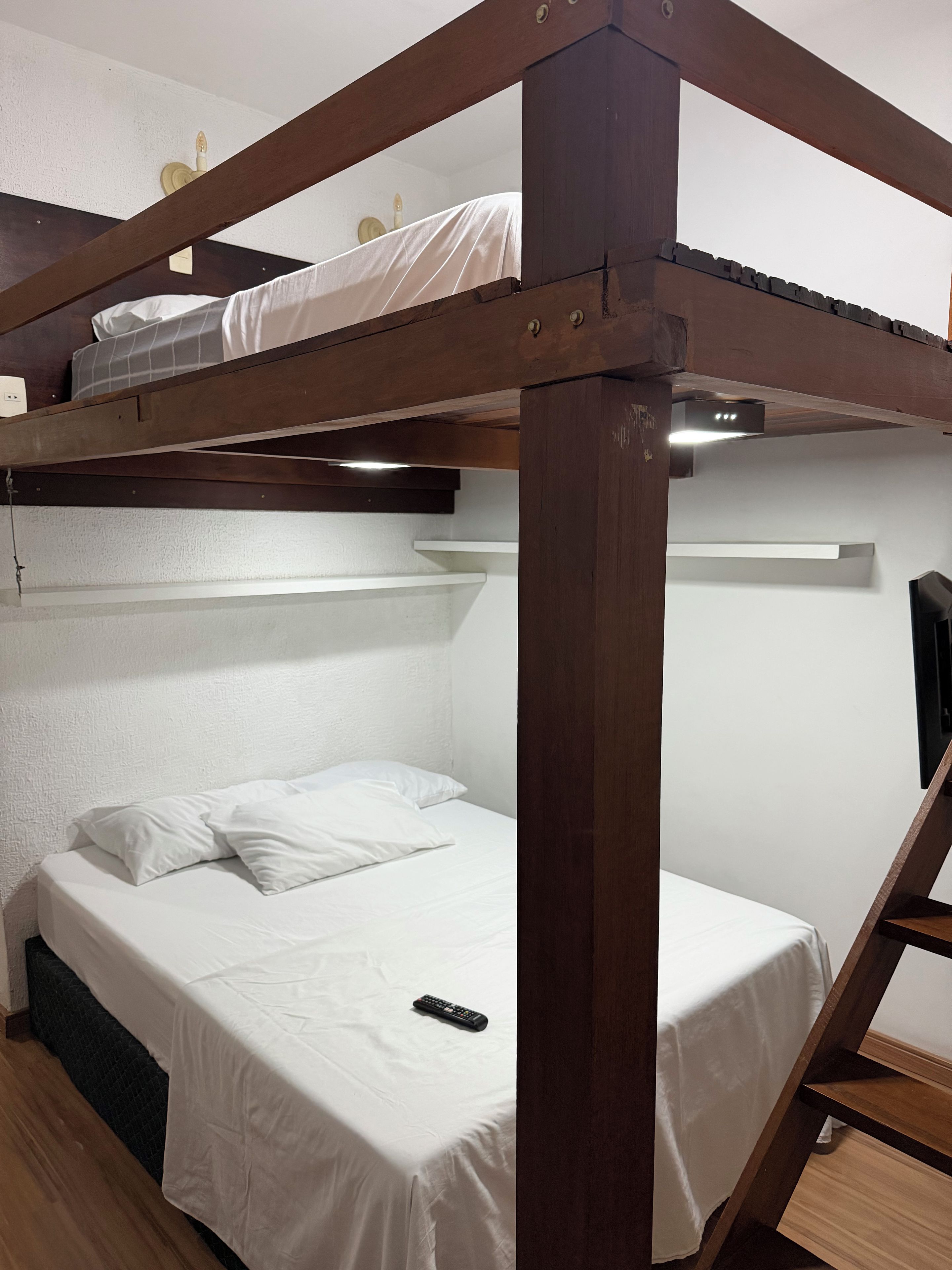 A bunk bed with white bedding and a remote control on the lower bed.