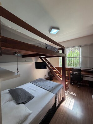 A bunk bed room with a desk and chair, a small fan, and a window with a view of greenery. - Smart & Cozy: Best Location in Botafogo | Steps to Metro & Shops | Sleeps 6 (Rio de Janeiro)