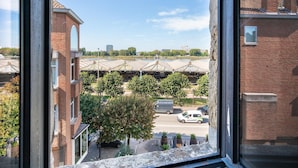 Blick aus einem Fenster auf einen Parkplatz mit einem Backsteingebäude, Bäumen und blauem Himmel.