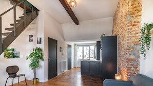 Ein geräumiger Wohnbereich mit Holzboden, einer Treppe, einer Küche mit Backsteinwand und einem blauen Sofa.