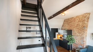 Eine Treppe mit schwarzen Geländern, eine Küchenzeile mit Backsteinwand und ein blaues Sofa.