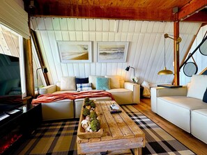 Ein gemütliches Wohnzimmer mit einem Holztisch, zwei weißen Sofas, einem karierten Teppich und gerahmten Kunstwerken an der Wand.