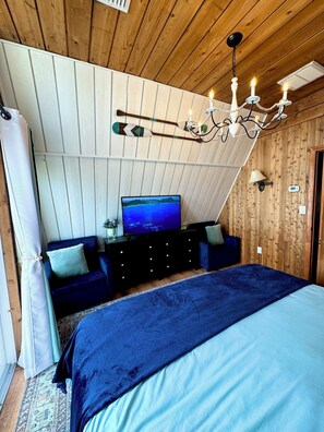 Ein Schlafzimmer mit Fernseher, Holzbalkendecke und einer Kristallleuchter.