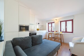 Ein gemütlicher Wohnraum mit Küchenzeile, einer Couch, einem Esstisch und einem Fenster mit Vorhängen.