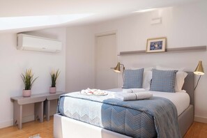 Ein Schlafzimmer mit Bett, Nachttischlampen, einem Schreibtisch, einer Topfpflanze und einer Wand-Klimaanlage.