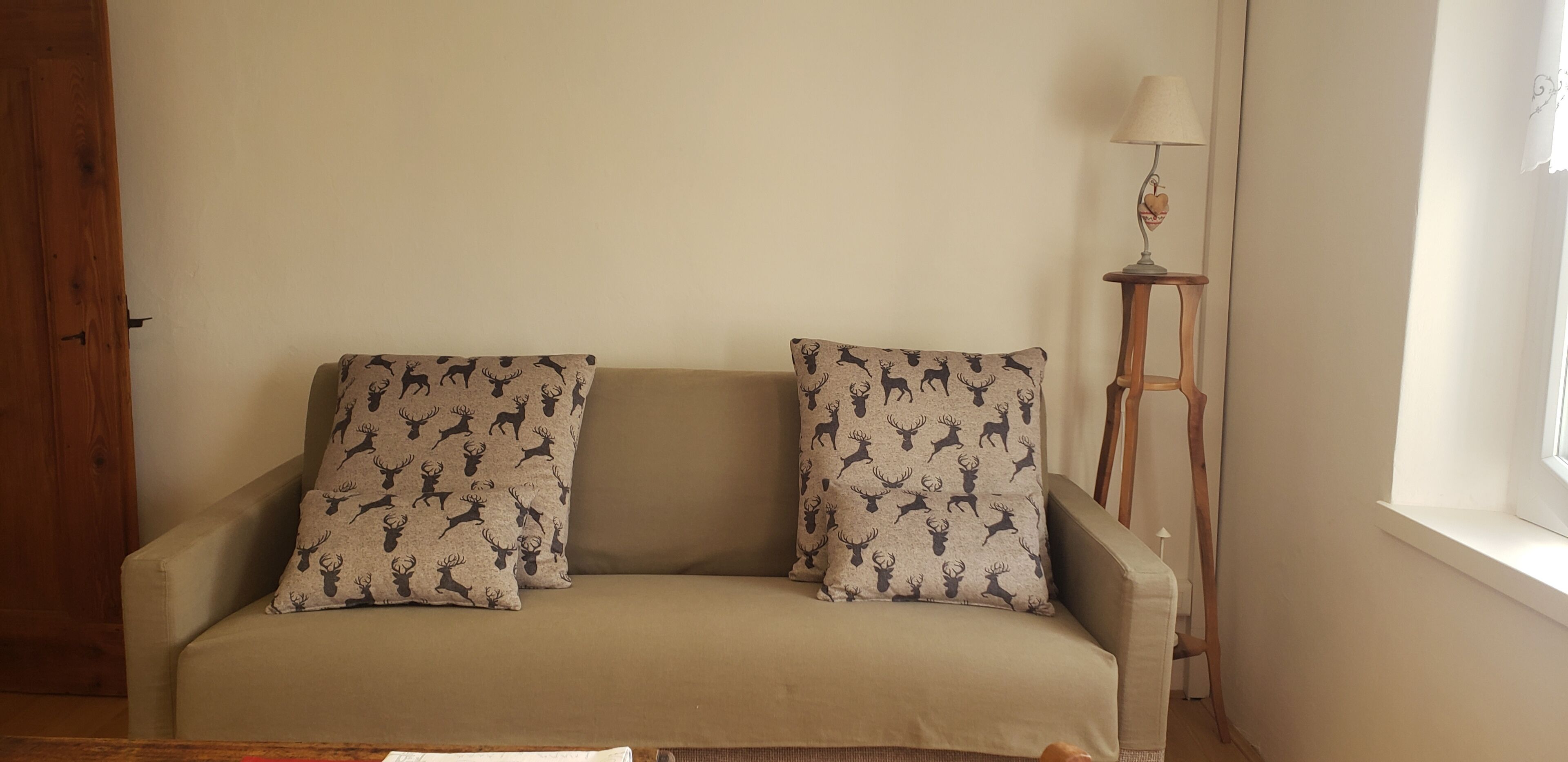 Un canapé beige agrémenté de coussins à motifs, un plancher en bois, une lampe et une fenêtre avec des rideaux.