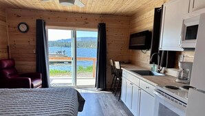 Huone, jossa on sänky, pieni keittiönurkkaus, televisio ja näkymä järvelle.