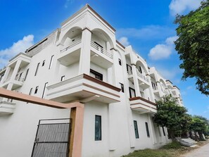 A multi-story building with balconies, a gated entrance, and a clear sky. - Classic With Balcony Chhatikara Char Dham (Mathura)
