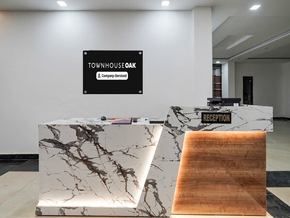 A reception desk with a marble top and a wooden accent piece, a sign above stating 'Townhouse Oak Company-Serviced,' and a reception area with a modern design. - Classic With Balcony Chhatikara Char Dham (Mathura)