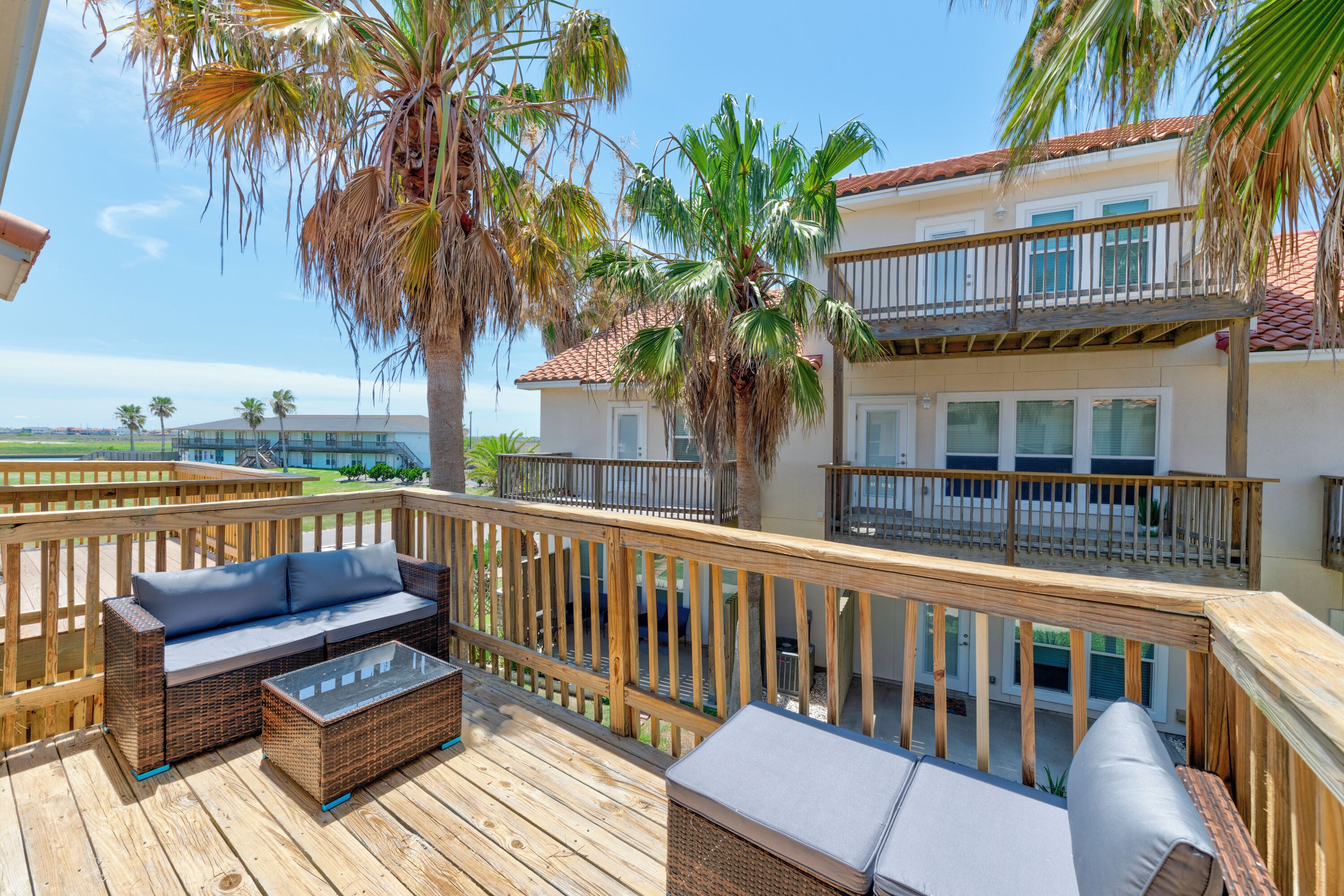 A wooden deck with outdoor furniture, a palm tree, and a building with a balcony.