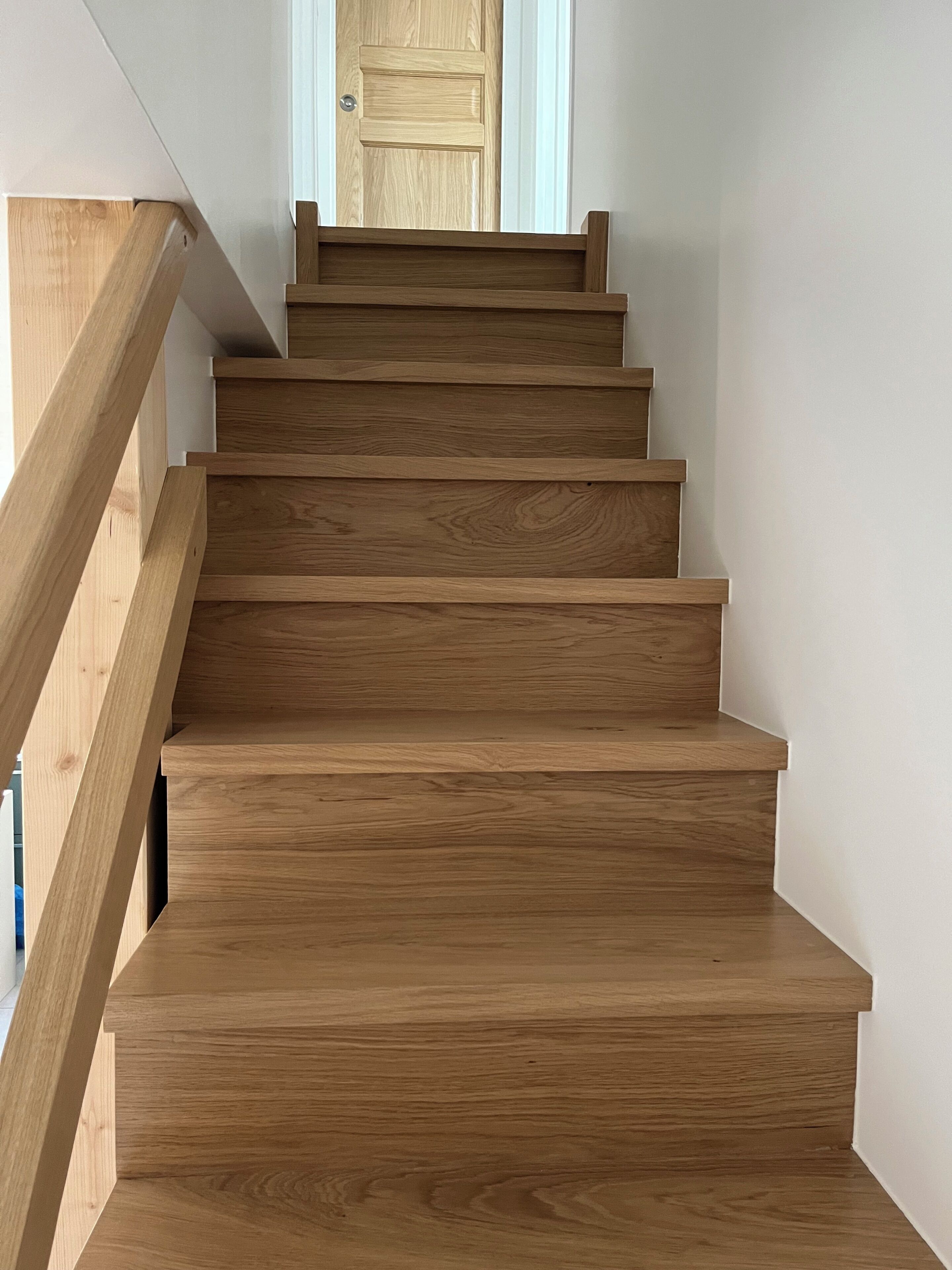 Una escalera de madera con barandilla que lleva a una puerta.