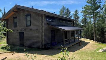 Une cabane en rondins avec un porche et une terrasse couverte.