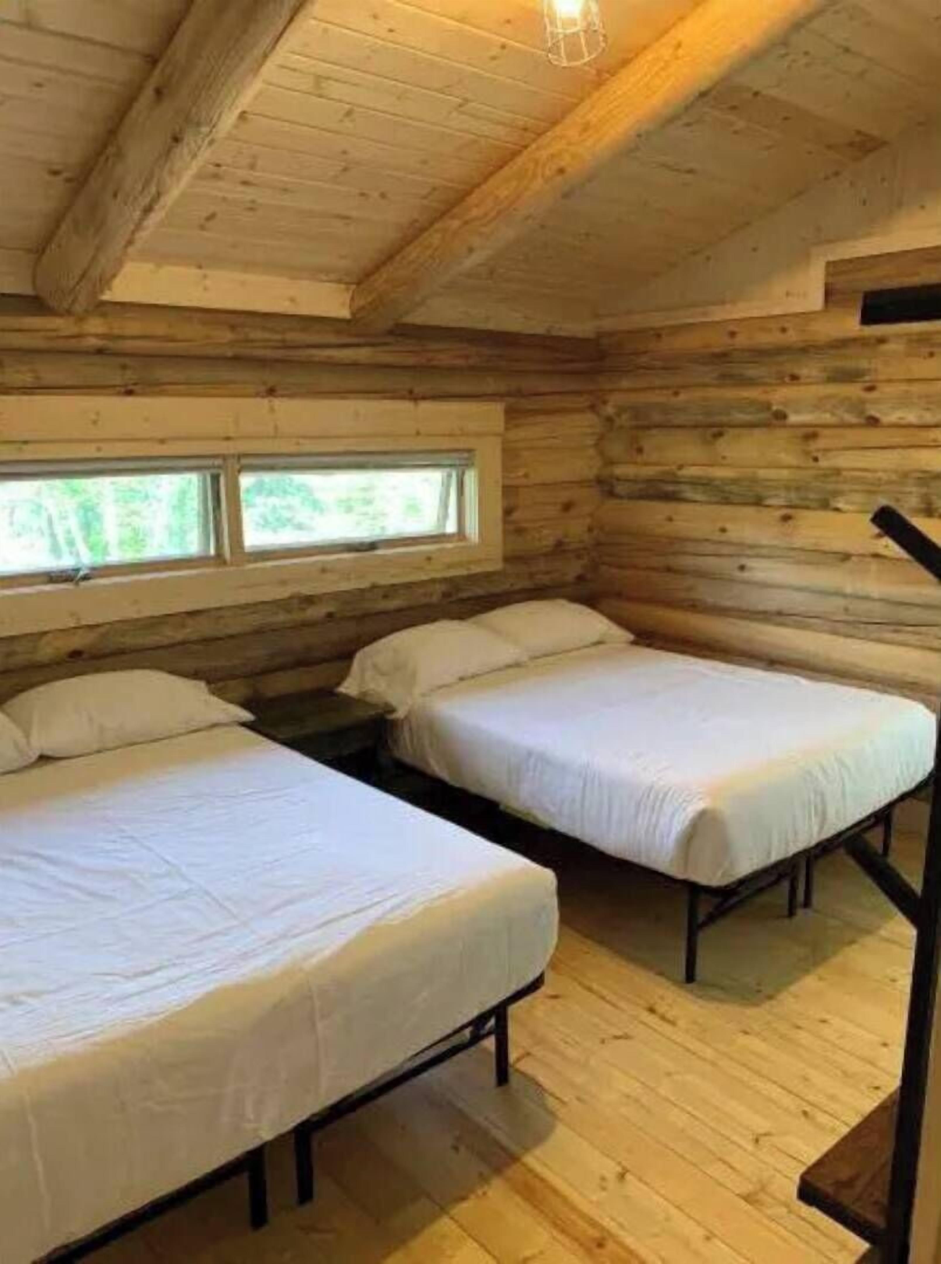 A cabin with two beds, wooden walls, and a window.