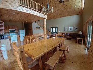 A wooden interior with a dining table, benches, a kitchen, a staircase, and a living area with a sofa and a lamp. - Spacious Cabin on the lake (Ely)