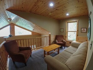 A cozy cabin interior with a wooden ceiling, a sofa, a chair, a small table, and a window. - Spacious Cabin on the lake (Ely)