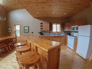 A wooden kitchen with a central island, wooden cabinets, a stove, and a refrigerator. - Spacious Cabin on the lake (Ely)