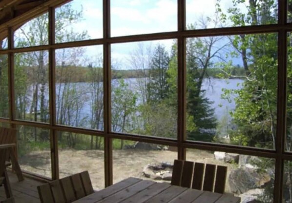 A covered outdoor seating area with a view of a lake and trees. - Spacious Cabin on the lake (Ely)