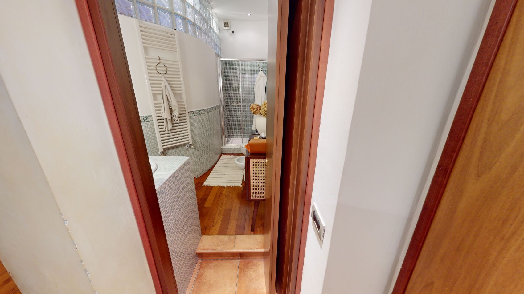Ein Flur, der zu einem Badezimmer mit Dusche, Toilette und Waschbecken führt.
