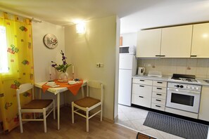 A compact kitchen with white cabinets, a stove, and a microwave. There is a dining table with chairs and a vase with flowers. - Holiday Garden Retreat (Umag)