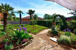 Ein Garten mit einem Kiesweg, Palmen und violetten Blumen.