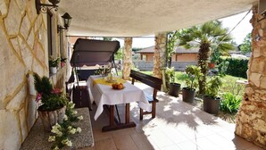 Un patio cubierto con una mesa, un banco, paredes de piedra, plantas en macetas y una parrilla.