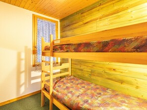 A bunk bed room with a wooden ceiling and walls, a patterned bedspread, and a window with patterned curtains. - Spacious Mountain Stay for 7 in Doucy (La Léchère)