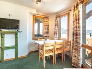 A room with a dining table, chairs, a television on a stand, and a window with curtains. - Spacious Mountain Stay for 7 in Doucy (La Léchère)