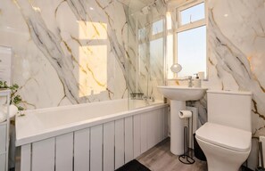 Een moderne badkamer met een marmeren wand, een badkuip, een wastafel en een toilet.