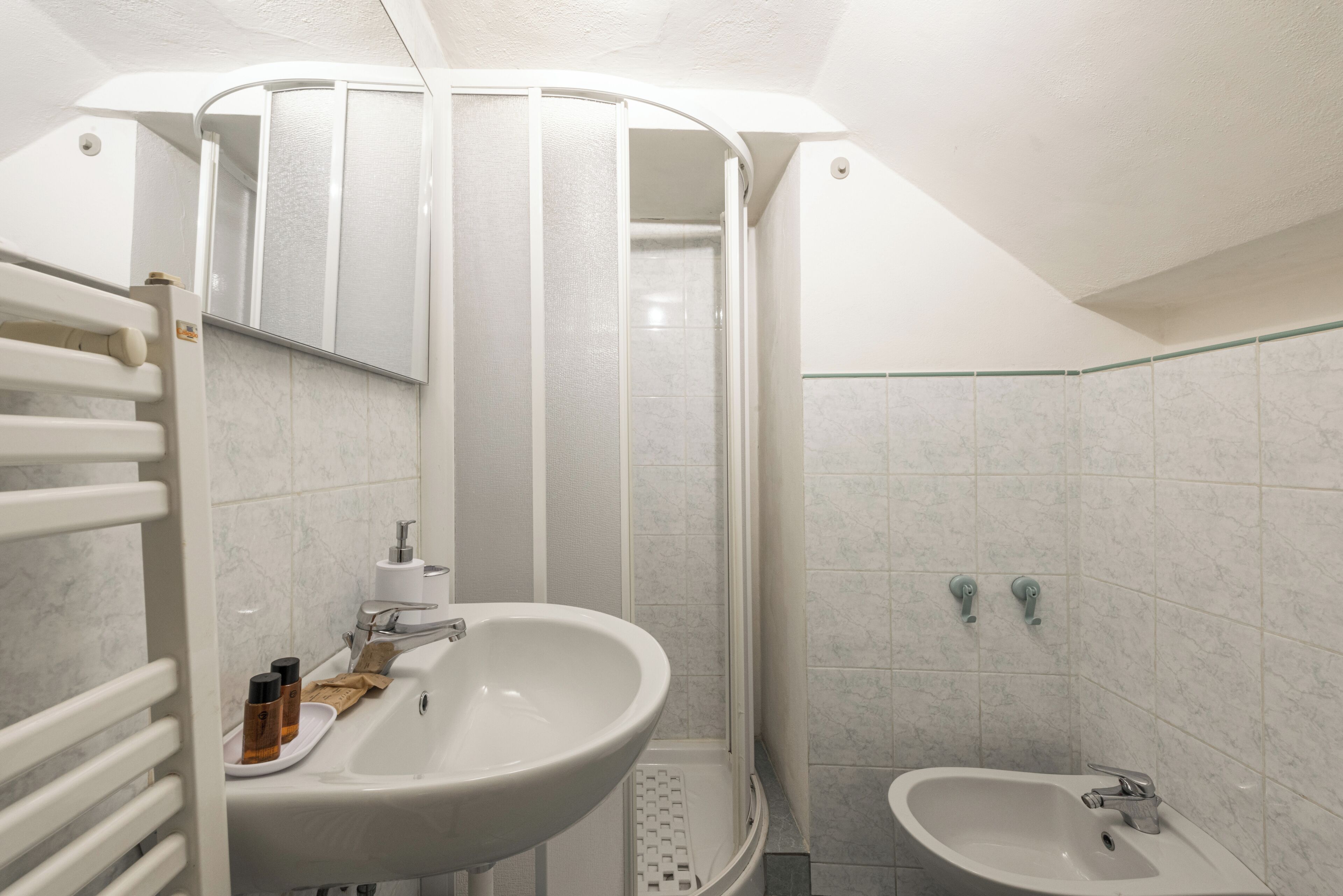 Un baño con ducha, dos lavamanos, un espejo y un perchero para toallas.