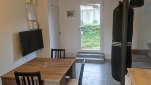 A room with a wooden dining table, chairs, a television mounted on the wall, a sofa, and a door leading to an outdoor area. - T2 Fully Equipped 4 Sleeps - Comfort and Proximity to Amenities (Réalmont)