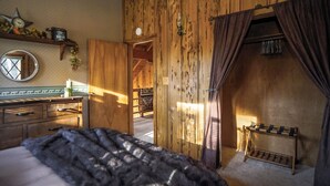 A wooden interior with a bed, a mirror, a shelf with items, and a coat rack.