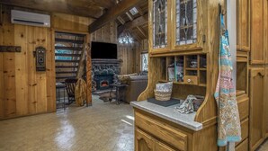 A wooden interior with a fireplace, a television, and a kitchen area with wooden cabinets and a hanging towel.