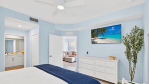 Una camera da letto con un letto, una cassettiera, un quadro raffigurante una spiaggia e una pianta.