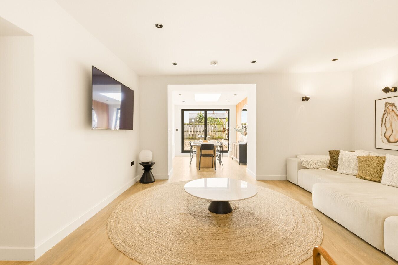 Un salon moderne avec un tapis rond, un canapé blanc, une table à manger et une vue sur une terrasse extérieure.