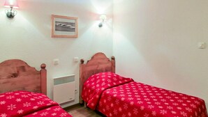 Une chambre à coucher avec deux lits en bois, un mur blanc, un tableau encadré et deux lampes fixées au mur.
