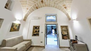 An interior with a stone ceiling, a doorway leading outside, a sofa, and a small cabinet. - Live the History: The timeless charm of an Ancient Dwelling in the heart of Maglie (Maglie)