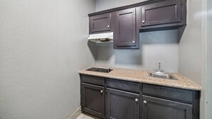 A compact kitchen with dark cabinets, a granite countertop, and a stainless steel sink. - Value Inn and RV Park (Baytown)