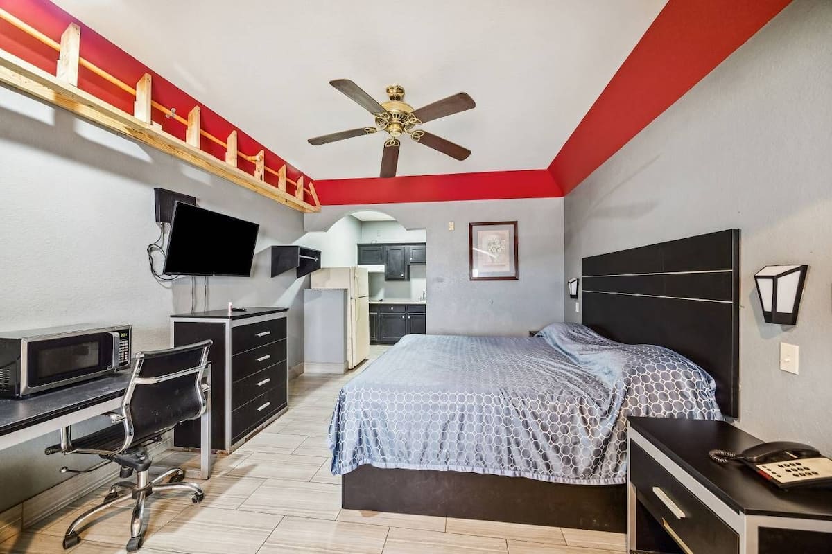 A bedroom with a bed, desk, chair, and a ceiling fan.