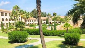 A hotel courtyard with palm trees, a pathway, and a building with arches. - Comfortable Seaview Stay for 8 (Linguizzetta)