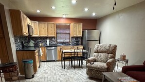 Una cocina con armarios de madera, una mesa de comedor con sillas, un sillón estampado, un sofá y una mesita auxiliar.