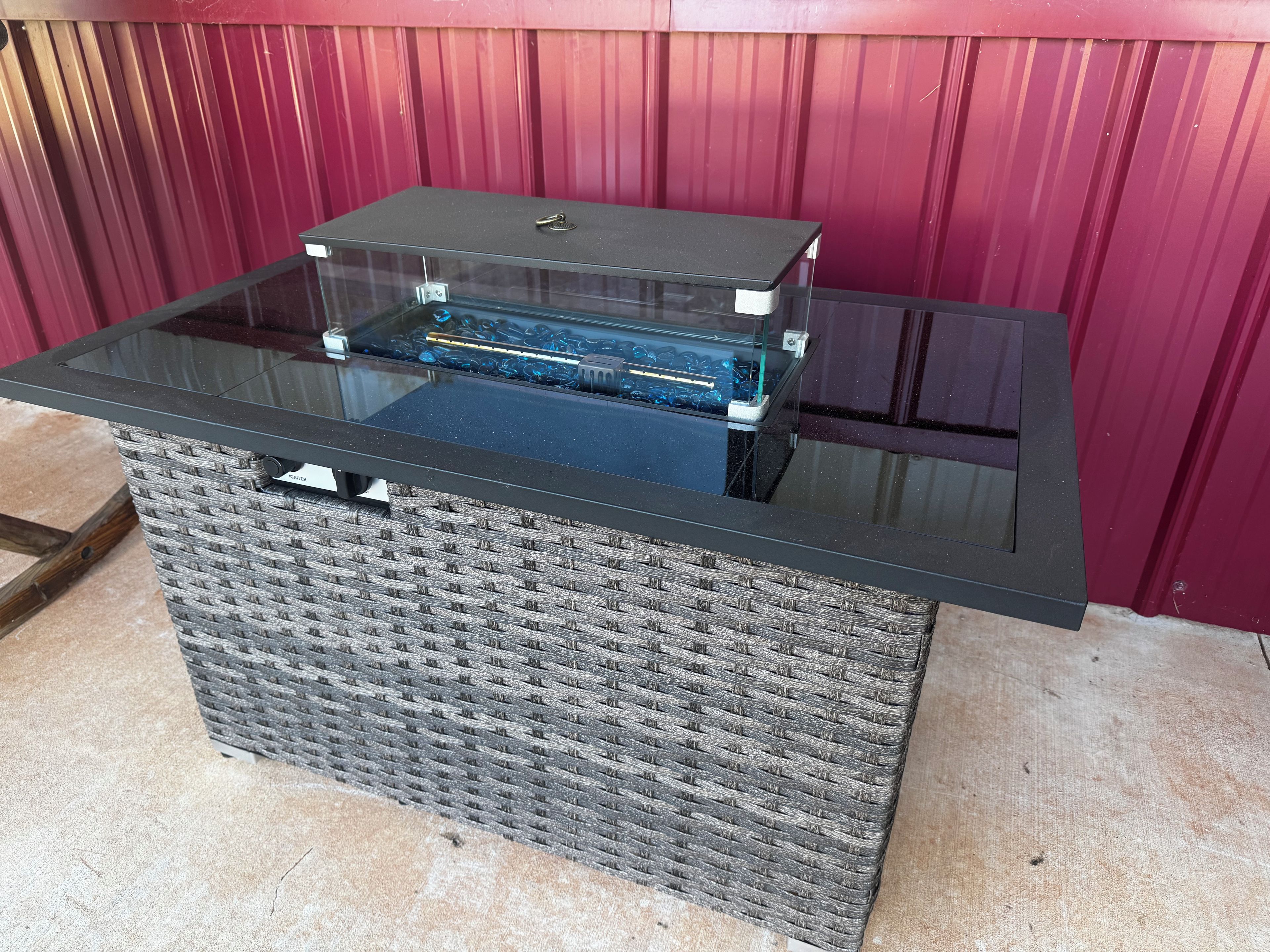 A rectangular outdoor storage unit with a glass top and wicker sides, against a red background.