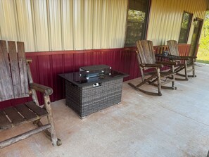 A covered outdoor seating area with wooden rocking chairs and a table with a glass top.