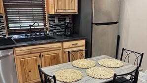 Una cocina con una mesa de comedor, sillas, un refrigerador y una cafetera.