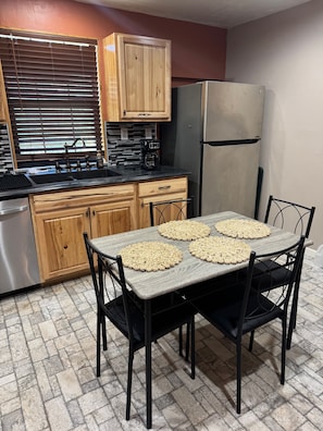 A kitchen with a dining table, chairs, a refrigerator, and a coffee maker.