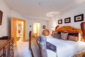 A bedroom with a wooden headboard, a bed with multiple pillows, a nightstand, a wooden dresser, and a chair. There are framed pictures on the wall and a door leading to another room. - Walk to Ski Slopes + Trails! Cozy 2-Bedroom, 3-Bath, Recently Renovated Condo with Pool, Hot Tub, BBQ, and A/C | BBL-251 by KBM Resorts (Park City)