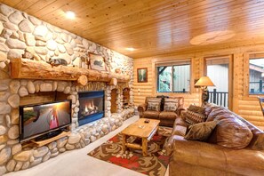 A log cabin interior with a stone fireplace, leather furniture, and a television. - Walk to Ski Slopes + Trails! Cozy 2-Bedroom, 3-Bath, Recently Renovated Condo with Pool, Hot Tub, BBQ, and A/C | BBL-251 by KBM Resorts (Park City)