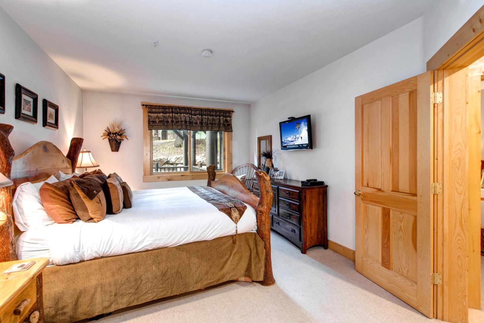 A bedroom with a bed, a dresser, a television, and a large wooden door.