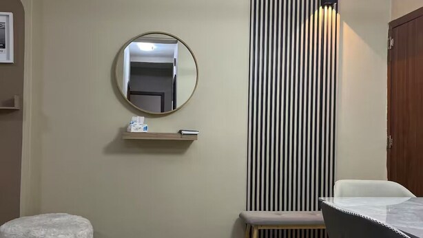 A modern room with a round mirror, a small shelf, a bench, a table, and a patterned rug. - COZY' HOME (conakry)