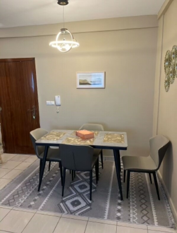 Un espace repas comprenant une table, des chaises, un tapis, un luminaire suspendu et un tableau encadré accroché au mur.
