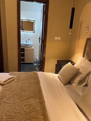 A hotel room with a bed, bedside table, and a view into the bathroom.